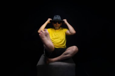 Olgun bir adam, 50 'li yaşlarda, sarı bir gömlek giyiyor ve otururken kafasına şapka takıp fotoğraf çektirmek için poz veriyor. Sınırsız kişi. Brezilya