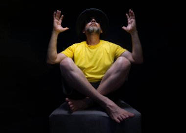 Olgun bir adam, 50 'li yaşlarda, sarı gömlek, güneş gözlüğü ve şapka takıyor, oturuyor, elleriyle poz veriyor. Şık bir insan. Brezilya