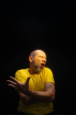 Olgun bir adam, 50 'li yaşlarda, kel ve sakallı, sarı gömlek giyiyor, el hareketleri yapıyor ve endişe, korku ya da rahatsızlık gösteriyor. Psikolojik bakım konsepti. Brezilya