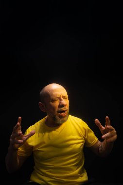 Olgun bir adam, 50 'li yaşlarda, kel ve sakallı, sarı gömlek giyiyor, el hareketleri yapıyor ve endişe, korku ya da rahatsızlık gösteriyor. Psikolojik bakım konsepti. Brezilya