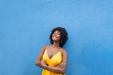 Sarı elbiseli, afro saçlı, mavi renkli bir duvarda izole edilmiş güzel bir kadın. Kendinden emin ve mutlu biri.