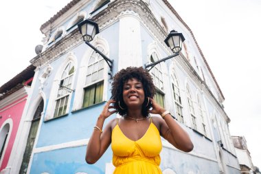 Sarı elbiseli güzel siyah bir kadın ve eski evin arka planında afro saç stili. Kendinden emin ve mutlu biri. Brezilya