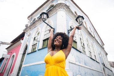 Sarı elbiseli güzel siyah bir kadın ve eski evin arka planında afro saç stili. Kendinden emin ve mutlu biri. Brezilya