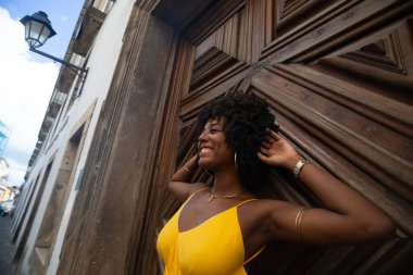 Yüzyıllık ahşap bir kapıya karşı, sarı bir elbise giyen, afro saçlı bir kadının yakın plan portresi. Kendine güvenen biri. Brezilya