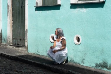 Cyan renkli bir duvarın yanında çömelmiş, yana bakan güzel bir kadının portresi. Seyahat eden biri. Güney Amerika.