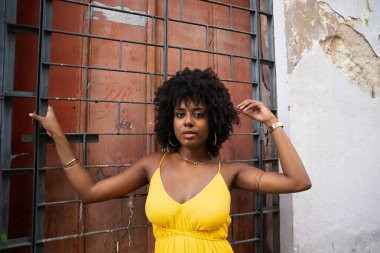 Sarı elbiseli, afro saçlı güzel bir kadın elinde kırmızı kapılı demir bir korkuluk tutuyor. Yolculukta kendine güveni olan biri.