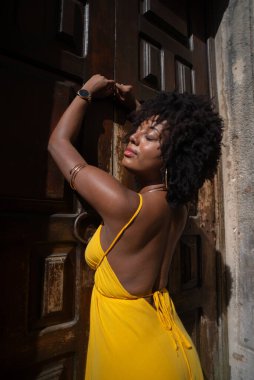 Sarı elbiseli güzel bir kadının portresi eski kahverengi ahşap kapının yanında duruyordu. Mutlu insan seyahat konsepti.