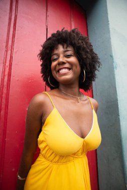 Kırmızı kapıya karşı sarı elbiseli ve afro saçlı güzel bir kadının yakın plan portresi. Kendinden emin ve mutlu biri. Brezilya