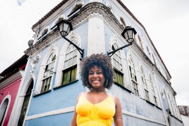 Sarı elbiseli güzel siyah bir kadın ve eski evin arka planında afro saç stili. Kendinden emin ve mutlu biri. Brezilya