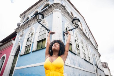 Sarı elbiseli güzel siyah bir kadın ve eski evin arka planında afro saç stili. Kendinden emin ve mutlu biri. Brezilya