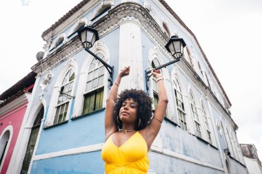 Sarı elbiseli güzel siyah bir kadın ve eski evin arka planında afro saç stili. Kendinden emin ve mutlu biri. Brezilya