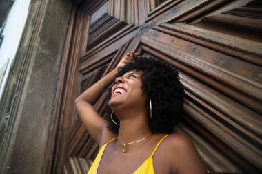 Yüzyıllık ahşap bir kapıya karşı, sarı bir elbise giyen, afro saçlı bir kadının yakın plan portresi. Kendine güvenen biri. Brezilya