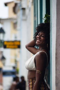 Arkası duvara dönük, fotoğraf için poz veren güzel siyahi bir kadının yarım boy fotoğrafı. Gülümseyen ve güçlü bir insan. Brezilya