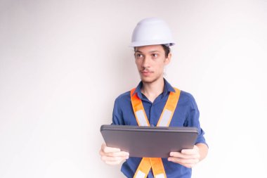 Genç mimar beyaz kask ve parlak yelek giyiyor, dizüstü bilgisayarla çalışıyor. Beyaz arka planda izole edilmiş. Güvenlik ekipmanları.