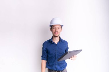 Beyaz kask ve parlak yelek giyen genç bir mimar dizüstü bilgisayar tutuyor ve kameraya bakıyor. Beyaz arka planda izole edilmiş. Güvenlik ekipmanları.