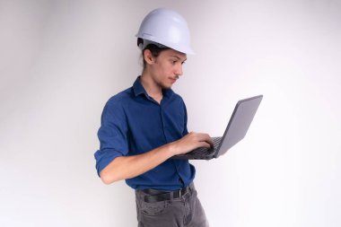 Genç mimarın portresi beyaz kask takıyor, dizüstü bilgisayarla çalışıyor. Beyaz arka planda izole edilmiş. Güvenlik ekipmanları.