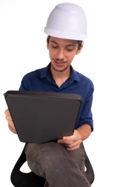 Genç mimar beyaz kask takıyor, oturuyor ve tabletle çalışıyor. Beyaz arka planda izole edilmiş. Güvenlik ekipmanları.