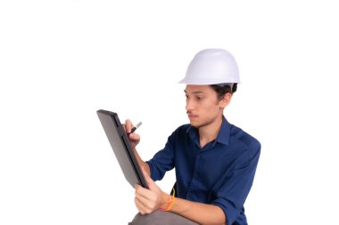 Genç mimar beyaz kask takıyor, oturuyor ve tabletle çalışıyor. Beyaz arka planda izole edilmiş. Güvenlik ekipmanları.