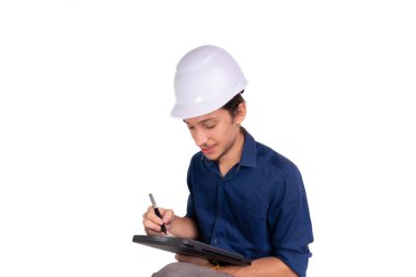 Genç mimar beyaz kask takıyor, oturuyor ve tabletle çalışıyor. Beyaz arka planda izole edilmiş. Güvenlik ekipmanları.