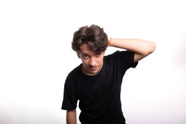 Siyah gömlekli yakışıklı genç adam, gülümsüyor, kameraya bakıyor ve elini saçına sokuyor. Sakin ve mutlu bir insan. Beyaz ırk.