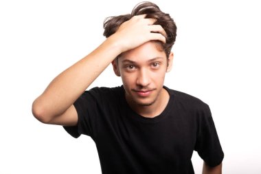 Siyah gömlekli yakışıklı genç adam, gülümsüyor, kameraya bakıyor ve elini saçına sokuyor. Sakin ve mutlu bir insan. Beyaz ırk.