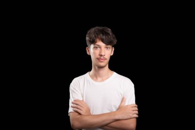 Beyaz gömlek giyen, gülümseyen, kollarını kavuşturup fotoğraf için poz veren genç yakışıklı bir adam. Siyah arka planda izole edilmiş. Stüdyo çekimi