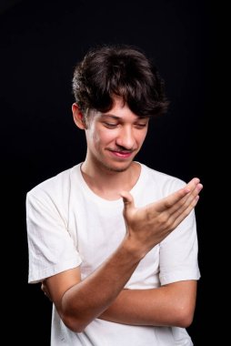 Beyaz gömlek giyen yakışıklı bir gencin yakından çekilmiş portresi eline bakıyor. Siyah arka planda izole edilmiş. Stüdyo çekimi