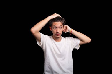 Beyaz gömlekli yakışıklı bir gencin portresi. Saçına elinle dokunuyor ve fotoğraf için poz veriyor. Siyah arka planda izole edilmiş. Kafkasya Brezilyası.