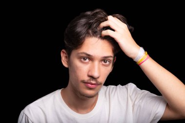 Beyaz gömlekli yakışıklı bir gencin portresi. Saçına elinle dokunuyor ve fotoğraf için poz veriyor. Siyah arka planda izole edilmiş. Kafkasya Brezilyası.