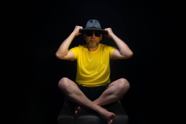 Olgun bir adam, 50 'li yaşlarda, sarı bir gömlek giyiyor ve otururken kafasına şapka takıp fotoğraf çektirmek için poz veriyor. Sınırsız kişi. Brezilya