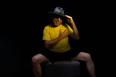 Olgun bir adam, 50 'li yaşlarda, sarı bir gömlek giyiyor ve otururken kafasına şapka takıp fotoğraf çektirmek için poz veriyor. Sınırsız kişi. Brezilya