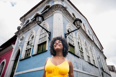 Sarı elbiseli güzel siyah bir kadın ve eski evin arka planında afro saç stili. Kendinden emin ve mutlu biri. Brezilya