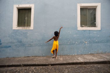 Sarı elbiseli ve afro saçlı güzel siyah bir kadın bir evin pencereleri arasında fotoğraf çekmek için poz veriyor. Kendinden emin ve mutlu biri. Brezilya