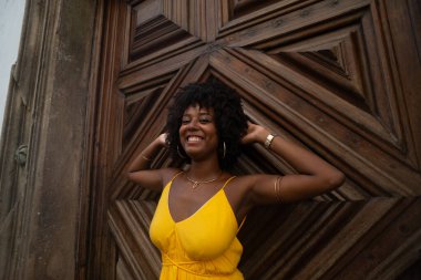 Yüzyıllık ahşap bir kapıya karşı, sarı bir elbise giyen, afro saçlı bir kadının yakın plan portresi. Kendine güvenen biri. Brezilya