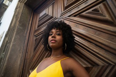 Yüzyıllık ahşap bir kapıya karşı, sarı bir elbise giyen, afro saçlı bir kadının yakın plan portresi. Kendine güvenen biri. Brezilya