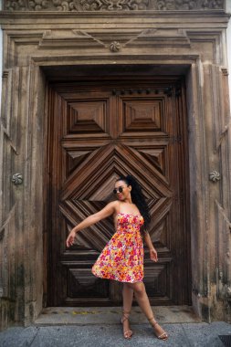 Örgülü ve renkli elbiseli genç beyaz kadın büyük, eski ahşap bir kapıya karşı kameraya poz veriyor. Seyahat eden biri. Brezilya