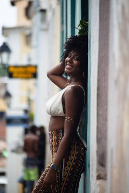 Arkası duvara dönük, fotoğraf için poz veren güzel siyahi bir kadının yarım boy fotoğrafı. Gülümseyen ve güçlü bir insan. Brezilya