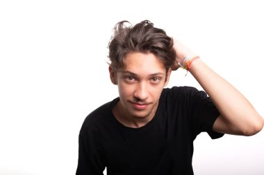 Siyah gömlekli yakışıklı genç adam, gülümsüyor, kameraya bakıyor ve elini saçına sokuyor. Sakin ve mutlu bir insan. Beyaz ırk.