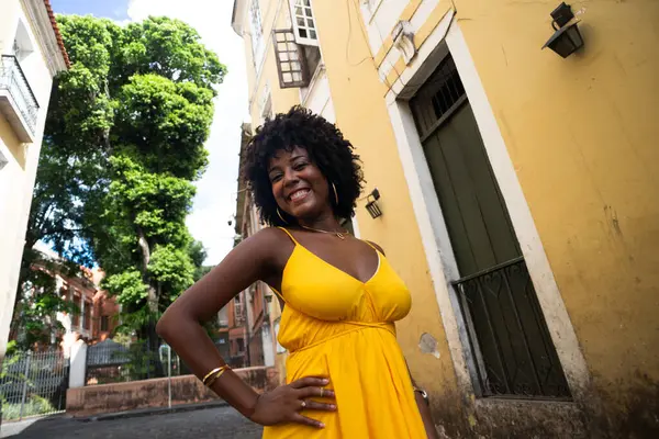 Güzel siyah bir kadın kaldırım taşı sokaklarda yürüyor sarı giysiler içinde, afro saçlı, gülümseyen ve mutlu. Yolculukta kendine güveni olan biri.