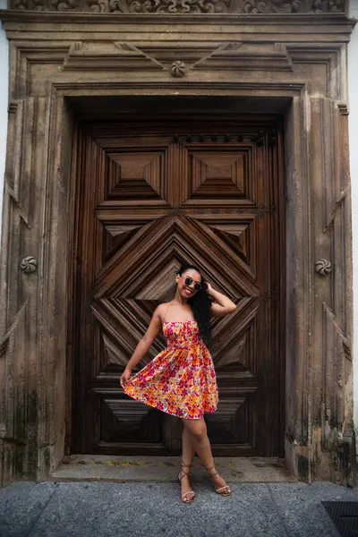 Örgülü ve renkli elbiseli genç beyaz kadın büyük, eski ahşap bir kapıya karşı kameraya poz veriyor. Seyahat eden biri. Brezilya