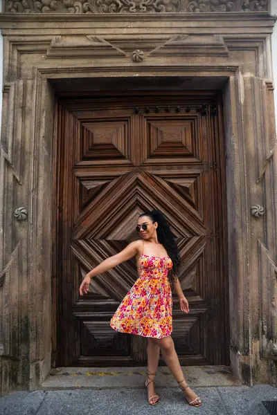 Örgülü ve renkli elbiseli genç beyaz kadın büyük, eski ahşap bir kapıya karşı kameraya poz veriyor. Seyahat eden biri. Brezilya