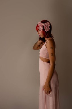 Genç, güzel, kızıl saçlı, pembe elbiseli, arka planda fotoğraf için poz veren bir kadın. Stüdyo resmi