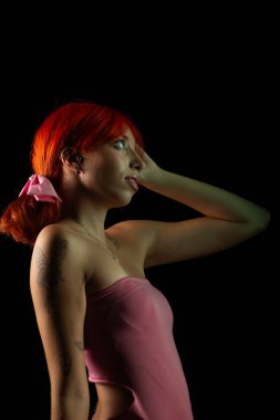 Güzel, genç, kızıl saçlı bir kadının portresi, oturan, pembe elbiseli, koyu arkaplanda fotoğraf için poz veren. Stüdyoda yapılmış bir portre.