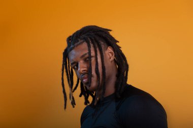 Siyah elbiseli yakışıklı bir gencin stüdyo portresi ve portakal renkli arka planda poz vermesi. Kendine güvenen ve sakin biri..