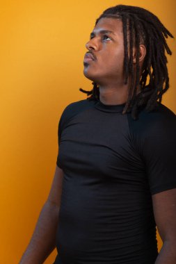 Siyah elbiseli yakışıklı bir gencin stüdyo portresi ve portakal renkli arka planda poz vermesi. Kendine güvenen ve sakin biri..