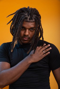 Siyah elbiseli yakışıklı bir gencin stüdyo portresi ve portakal renkli arka planda poz vermesi. Kendine güvenen ve sakin biri..