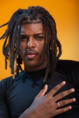 Siyah elbiseli yakışıklı bir gencin stüdyo portresi ve portakal renkli arka planda poz vermesi. Kendine güvenen ve sakin biri..