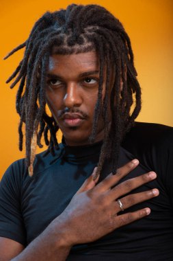 Siyah elbiseli yakışıklı bir gencin stüdyo portresi ve portakal renkli arka planda poz vermesi. Kendine güvenen ve sakin biri..