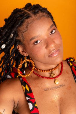 Saçları örgülü, geleneksel kıyafetler giyen ve kameraya poz veren güzel bir kadının dikey yakın plan portresi. Hardal renkli arka planda izole edilmiş. Kendine güvenen ve sakin biri..