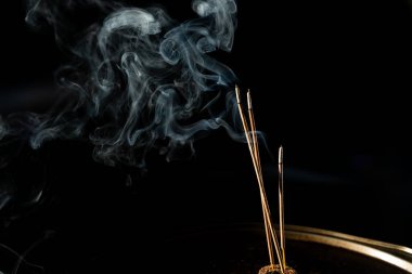 Siyah arka planda duman olan üç yanan tütsü çubuğu. Stüdyo çekimi.